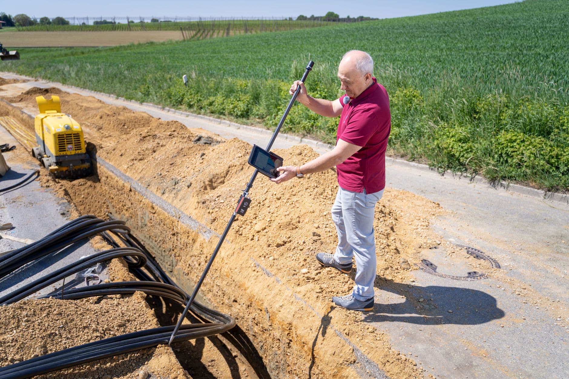 Adult male engineer using surveying equipment at a trench site on a sunny day.